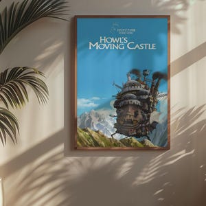 May include: A framed poster featuring the animated film "Howl's Moving Castle." The artwork depicts the castle with a blue sky background and mountains. The poster is in a wooden frame and hangs on a wall.