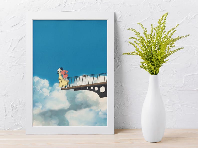 May include: A framed art print featuring an animated scene of two figures embracing on a bridge against a blue sky and cloud backdrop. The print is in a white frame, with a white vase holding green foliage to the right.