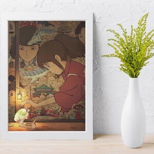 May include: A framed print of an animated film scene. It shows a girl in a red outfit, interacting with a small figure near a table. The background features other characters and a detailed, colourful landscape.