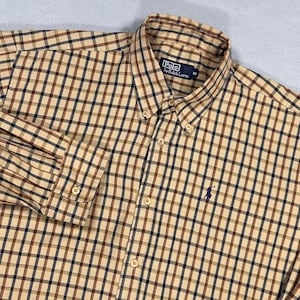 Könnte beinhalten: Ein langärmeliges Hemd mit Knopfleiste und einem karierten Muster in Beige, Braun und Marineblau. Das Hemd hat einen Button-Down-Kragen, eine durchgehende Knopfleiste und ein marineblaues gesticktes Logo auf der Brust. Das Etikett am Kragen zeigt Polo by Ralph Lauren.