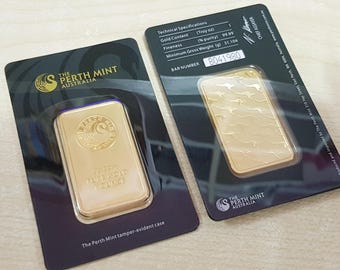 Puede incluir: Dos lingotes de oro en estuches a prueba de manipulaciones de The Perth Mint Australia. Cada barra es rectangular, con un acabado dorado y detalles en relieve. El embalaje incluye especificaciones técnicas, incluido el contenido de oro y el peso de 31,104 gramos.