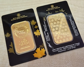 Puede incluir: Dos lingotes de oro de la Real Casa de la Moneda Canadiense, cada uno en un soporte negro con diseños de hojas de arce doradas. Las barras están estampadas con el logotipo de la casa de la moneda, un peso de 31,1035g y un número de serie.