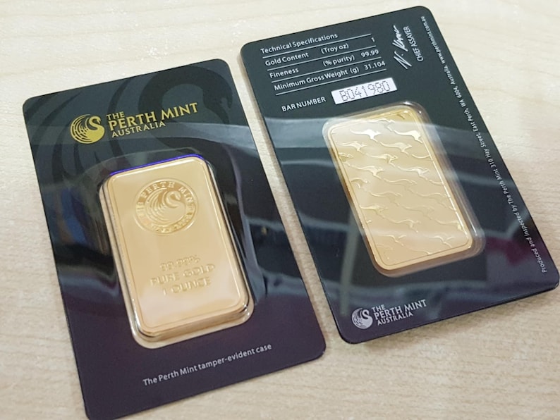 Pode incluir: Duas barras de ouro em embalagens inviol&aacute;veis da The Perth Mint Australia. Cada barra &eacute; retangular, com as palavras "1 Troy Ounce" e um logotipo. A embalagem inclui especifica&ccedil;&otilde;es t&eacute;cnicas, incluindo o n&uacute;mero da barra.