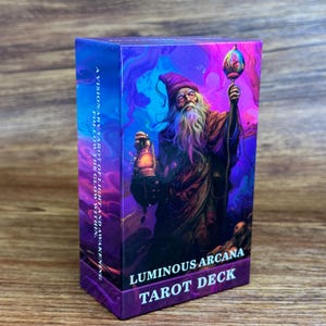 以下が含まれることがあります： Luminous Arcana Tarot Deckと書かれた長方形のタロットカードボックス。箱には、ランタンと光るオーブを持つ、とんがり帽子をかぶった髭の人物が描かれています。テキストは「A visionary tarot of light and awakening follow the glow within.」と書かれています。