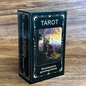 Könnte beinhalten: Eine schwarze, rechteckige Tarotkarten-Box mit weißen, himmlischen Randverzierungen. Die Vorderseite zeigt das Wort TAROT, den Text Renaissance painting theme und eine Illustration einer Figur auf einem Thron. Die Seite zeigt 78 Tarot Cards.