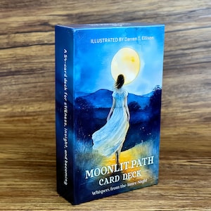 May include: A rectangular card deck box titled Moonlit Path Card Deck, Whispers from the Inner Night. The box features an illustration of a figure in a white dress walking toward a large yellow moon over blue hills, with text by Darren T. Ellison.