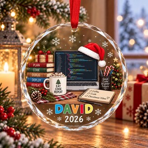 May include: A round, clear acrylic Christmas ornament featuring a laptop with code on the screen, a Santa hat, a mug labeled 'EAT CODE REPEAT', a stack of books, a notepad with a checklist, a small tree, and the text 'DAVID 2026' in colorful letters.