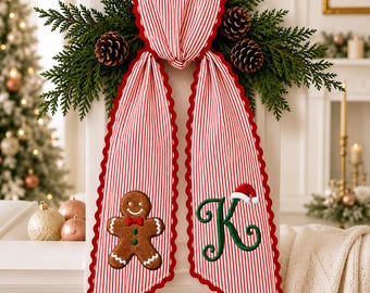 May include: A decorative fabric swag featuring red and white vertical stripes with a scalloped red edge. The left side displays an embroidered gingerbread man, while the right side features a large green letter K topped with a small Santa hat.