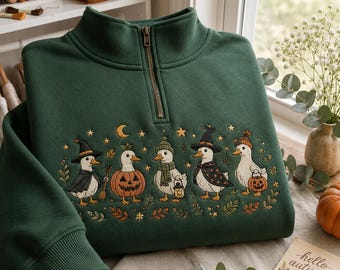 May include: A dark green quarter-zip sweatshirt featuring an embroidered design of five white ducks dressed in Halloween costumes, including a witch, a pumpkin, a scarf-wearing duck with a lantern, a wizard, and a duck holding a pumpkin bucket.