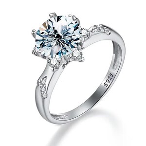 May include: A silver-toned ring featuring a large, round, faceted clear stone at the center, accented by smaller clear stones set along the prongs and the band. The interior of the band is clearly engraved with the hallmark S925 for sterling silver.