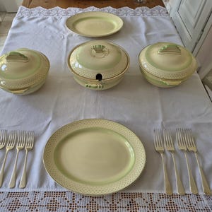 May include: A dinnerware set featuring two round lidded serving bowls with handles, one large oval platter, one smaller oval plate, and eight silver-toned metal forks. The ceramic pieces are pale green with a subtle dotted pattern along the edges.