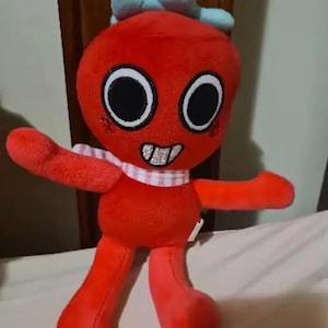May include: A red plush toy with a round head, large black eyes, and a wide mouth showing white teeth. It features a light blue bow on top of its head and a pink and white checkered scarf around its neck. The toy has long arms and legs.