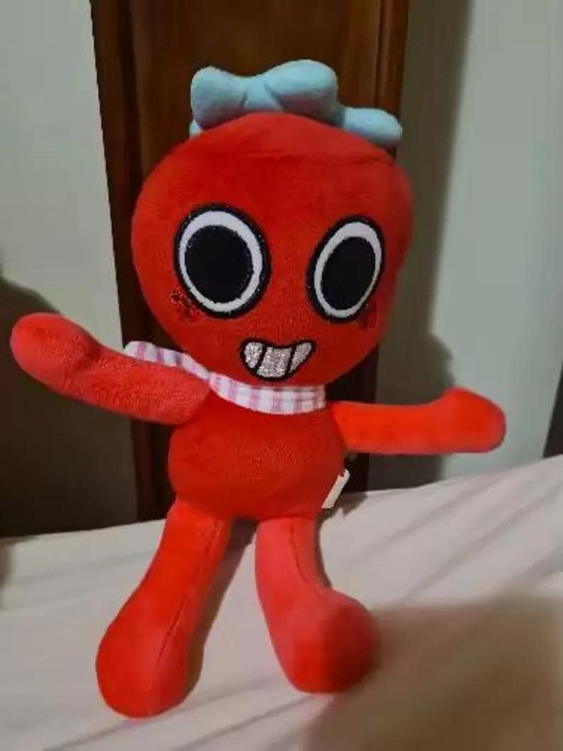 May include: A red plush toy with a round head, large black eyes, and a wide mouth showing white teeth. It features a light blue bow on top of its head and a pink and white checkered scarf around its neck. The toy has long arms and legs.