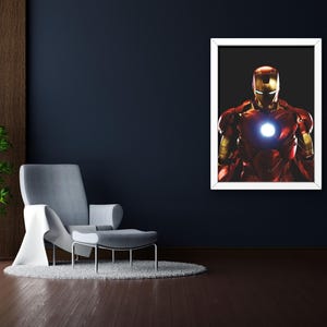 以下が含まれることがあります： 象徴的な赤と金のアーマーを着たアイアンマンが描かれた額入りのアートワーク。胸には光る部分があります。画像は白いフレームの中の黒い背景にあり、濃い青色の壁に取り付けられています。部屋には灰色のアームチェア、オットマン、鉢植えの植物があります。