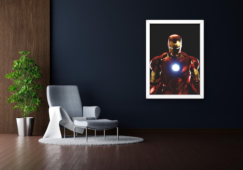 以下が含まれることがあります： 象徴的な赤と金のアーマーを着たアイアンマンが描かれた額入りのアートワーク。胸には光る部分があります。画像は白いフレームの中の黒い背景にあり、濃い青色の壁に取り付けられています。部屋には灰色のアームチェア、オットマン、鉢植えの植物があります。