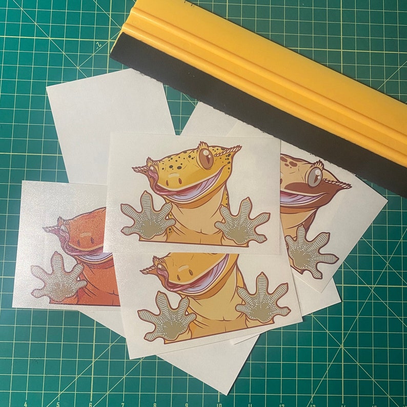 May include: Four sticker sheets featuring cartoon gecko illustrations. Each sheet has a different coloured gecko with a smiling face and a textured background.