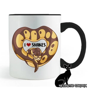 Peut inclure: Une tasse à café en céramique blanche avec une anse noire. La tasse présente une image de dessin animé d'un serpent enroulé en forme de cœur avec le texte "J'aime les serpents" dans un cœur rouge.