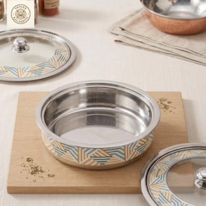 May include: Stainless steel serving bowl with a geometric pattern in blue, yellow, and white. The bowl sits on a wooden cutting board, with a matching lid nearby. The bowl is part of a kitchenware set.