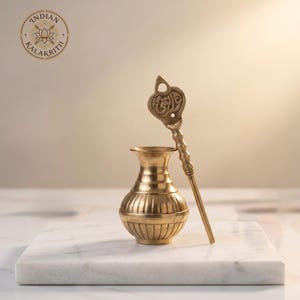May include: A brass-colored decorative vessel with a matching spoon-like tool. The vessel has a ribbed design and a flared top. The tool has an ornate handle and a decorative top. The image includes the text "INDIAN KALAKRITI" and a lotus flower logo.