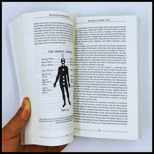 May include: Open book showing text and a diagram of the human body's energy centres. The diagram is a black silhouette with labelled points. The text discusses consciousness and energy.