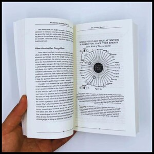 May include: An open book with text on both pages. The left page has the title "Where Attention Goes, Energy Flows." The right page has a diagram and the title "Where You Place Your Attention Is Where You Place Your Energy."