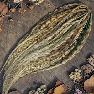May include: A collection of blonde, green, and brown dreadlocks with various textures, including braids and wavy strands. The dreadlocks are arranged on a rustic wooden surface, surrounded by dried flowers and autumn leaves.