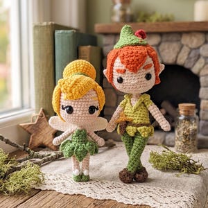 May include: Two amigurumi dolls crafted from yarn. One doll features yellow hair in a bun, white wings, and a green leaf-style skirt. The other doll has orange hair, a green pointed hat with a red accent, and a green tunic with brown shoes.