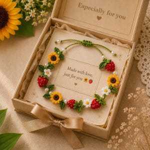 Peut inclure: Un bracelet crocheté fait main orné de tournesols, fraises et marguerites, présenté dans un coffret cadeau. Le bracelet est orné de perles et de feuilles vertes. Le coffret contient une carte avec le texte "Made with love, just for you."