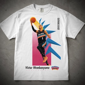 May include: White t-shirt featuring a graphic of a basketball player in a black and teal uniform, holding a basketball. The text "Victor Wembanyama" and "Spurs" are visible. The shirt also has the text "SKYBOX" on the right side.