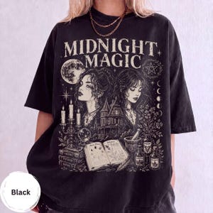Puede incluir: Una camiseta negra de manga corta con un estampado gráfico blanco que incluye el texto MIDNIGHT MAGIC. El diseño muestra a dos mujeres, una casa encantada, una luna llena, un pentagrama, velas, una bola de cristal, libros y frascos.