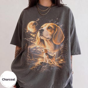 May include: A charcoal grey short-sleeve t-shirt featuring a graphic print of a beagle dog. The design includes a large beagle portrait above a smaller beagle standing on a rocky cliff near a lake, mountains, a full moon, and a lantern.