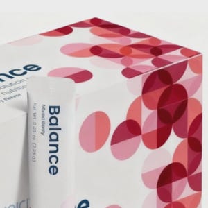Puede incluir: Un tubo blanco con la etiqueta "Balance" con sabor a "Mixed Berry" y un peso neto de 7,09 g. El tubo est&aacute; delante de una caja blanca con un patr&oacute;n de c&iacute;rculos rojos y rosas superpuestos. La palabra "nce" es parcialmente visible en la caja.