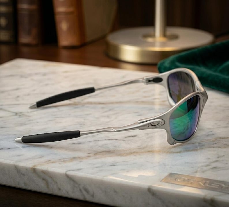 May include: Silver-framed sunglasses with black temple tips and reflective lenses. The lenses have a green and blue hue. The sunglasses are resting on a marble surface.