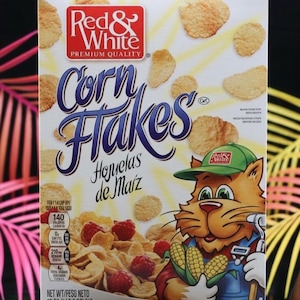 Peut inclure: Une boîte de céréales Corn Flakes Red & White. La boîte présente un chat de dessin animé tenant du maïs, avec les mots "Corn Flakes" en grandes lettres bleues. La boîte comprend également des informations nutritionnelles et le poids net de 510g.
