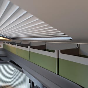 Pode incluir: Vista interior do painel de instrumentos de um veículo, com uma fila de compartimentos de armazenamento verdes e brancos acima do para-brisa. Um para-sol plissado é parcialmente visível, juntamente com o volante e o painel.