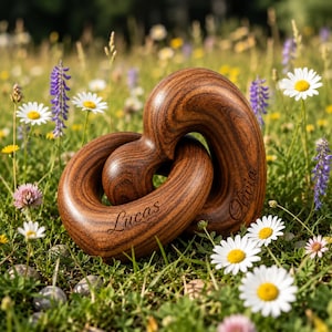May include: A wooden sculpture in the shape of two intertwined hearts, engraved with the names "Lucas" and "Olivia." The sculpture is made of dark brown wood and sits in a field of wildflowers, including daisies and purple lupine.