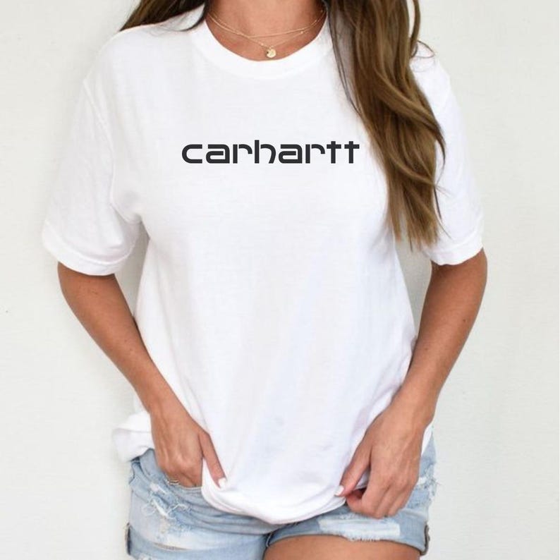 May include: A white short-sleeved t-shirt featuring the word carhartt printed in black lettering across the chest. The garment has a crew neckline and a relaxed fit, paired with light blue denim shorts that have a distressed, frayed hemline.