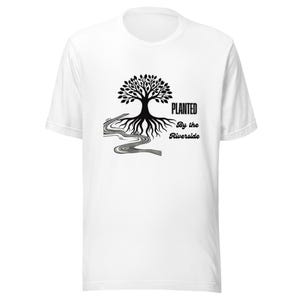 May include: White t-shirt featuring a black tree graphic with roots and a river design. The text "PLANTED By the Riverside" is printed in black. The shirt has a crew neck and short sleeves.