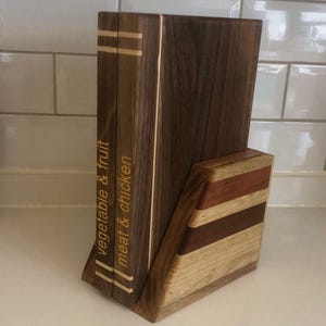 Könnte beinhalten: Ein Kochbuchhalter aus Holz mit dunkler brauner Oberfläche. Der Halter hat zwei vertikale Abschnitte mit den Wörtern "vegetable & fruit" und "meat & chicken" in heller Farbe. Der Sockel besteht aus hellem Holz mit Streifen.