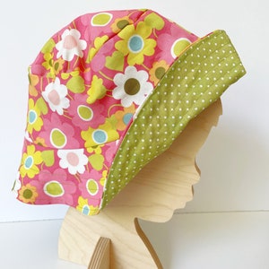 May include: A pink and green sun hat with a floral print and white polka dots. The hat is made of fabric and has a wide brim.