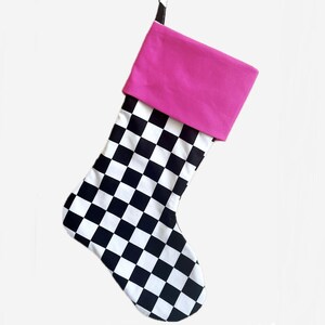 May include: A Christmas stocking with a black and white checkered pattern on the main body. The cuff is a solid bright pink color. A black loop is attached for hanging.
