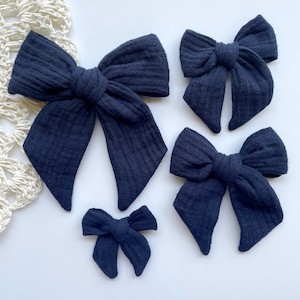 May include: Four navy blue fabric hair bows of different sizes. The bows are made of a soft, textured fabric and are tied in a classic bow shape.