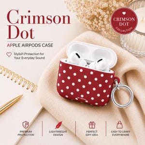 May include: A crimson red Apple AirPods case featuring a white polka dot pattern and a silver metal ring attachment. The case is open, revealing white wireless earbuds inside. Text on the case includes Crimson Dot, Apple Airpods Case, and N9 Design.