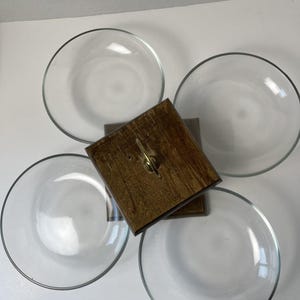 May include: A square wooden base with a central brass handle, surrounded by four clear glass bowls arranged in a circular pattern. The wooden base features a dark brown finish and a metallic handle centered on the top surface for easy carrying.
