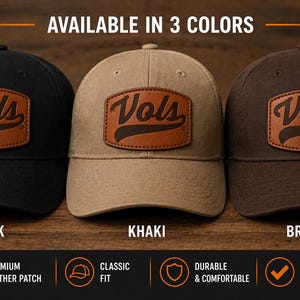 May include: Three baseball caps in black, khaki, and brown, each with a leather patch featuring the word "Vols". The caps are displayed on a wooden surface, with the text "AVAILABLE IN 3 COLORS" at the top.