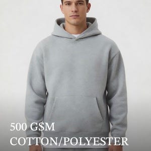 May include: A light gray heavyweight hoodie featuring a hood, long sleeves, and a front kangaroo pocket. The text 500 GSM COTTON/POLYESTER HEAVYWEIGHT is printed on the image. The garment is made of a cotton and polyester blend fabric.