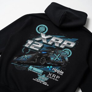 Puede incluir: Una sudadera negra con capucha que presenta un gran gráfico en la parte posterior. El diseño incluye un coche de carreras, el texto XRP 12, Ripple Labs, XRP Ecosystem y la frase The Standard for Digital Assets en tonos azules, blancos y plateados.