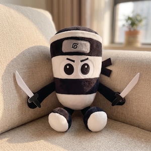 Puede incluir: Un peluche de ninja con un diseño de rayas blancas y negras. El juguete tiene una diadema negra con un emblema gris, brazos y piernas negros, y sostiene dos cuchillos de juguete blancos. El juguete ninja está sentado en un sofá beige.