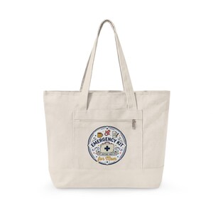 May include: Cream-colored canvas tote bag with a front pocket and zipper. The bag features a circular patch with the words "Emergency Kit for Mom" and various medical and baby-related icons. The bag has two long handles.