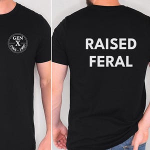 Op de afbeelding: Een zwart t-shirt met korte mouwen en een witte cirkelvormige afbeelding op de linkerborst met de tekst GEN X 1965-1980. De achterkant van het shirt toont de witte tekst RAISED FERAL in een vet, schreefloos lettertype.